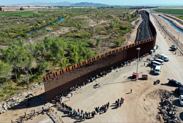 Immigrants wait in line to be processed by the U.S. Border Patrol after crossing through a gap in the U.S.-Mexico border barrier in Yuma, Ariz. on May 21, 2022.
