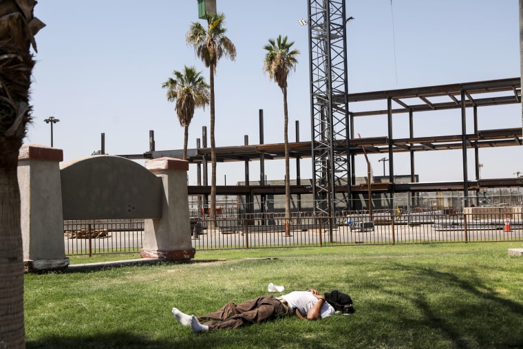 A man lies on the grass as the temperature reaches 115 degrees on June 12, 2022, in Calexico, Calif.