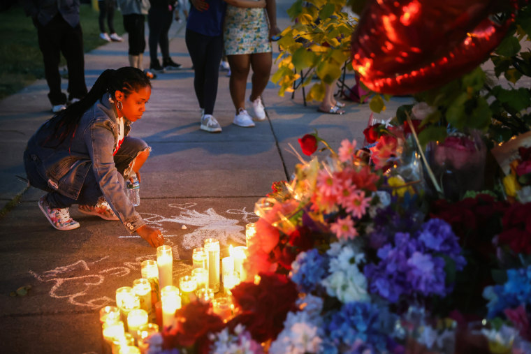 Image: A woman chalks a message at a makeshift memorial outside of the scene of a mass shooting at a Tops Friendly Markets location on May 15, 2022 in Buffalo, N.Y.
