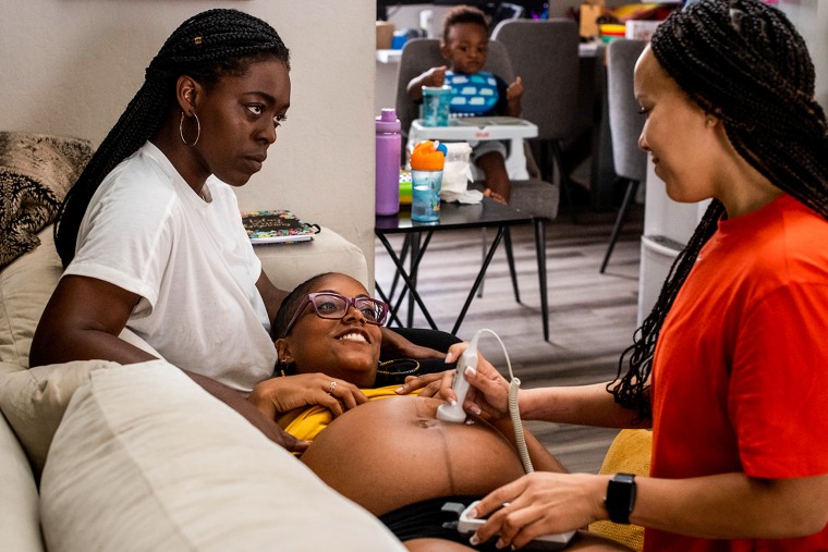 Image: Midwife Angie Miller, right, listens to the heart beat of MyLin Stokes Kennedys baby, center, with her wife Lindsay and their child Lennox, 21 months, in California on June 29, 2021. Black women are turning to midwives to avoid racism, mortality rates and unnecessary C-sections in the hospitals.