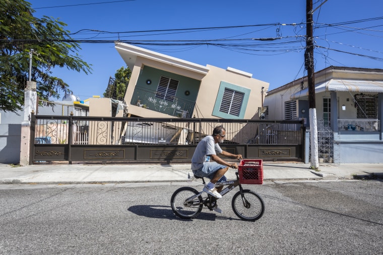 A man rides his bike in front of a collapsed house in Guanica, Puerto Rico