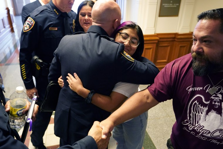 Jazmin Cazares es abrazada por el jefe de policía de Fort Worth, Neil Noakes, mientras ella y sus padres, Javier, a la derecha, y su madre, Gloria, en la parte de atrás, visitan a un grupo de jefes de policía después de una audiencia en el capitolio del estado, el jueves 23 de junio de 2022, en Austin, Texas.