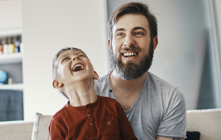 Father and son sitting together on the couch playing computer game