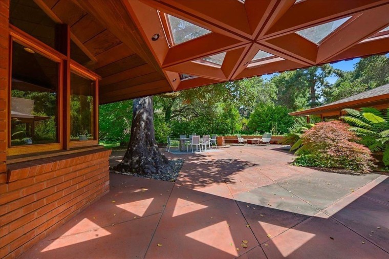 A large patio is surrounded by mature oak trees and pretty plants.