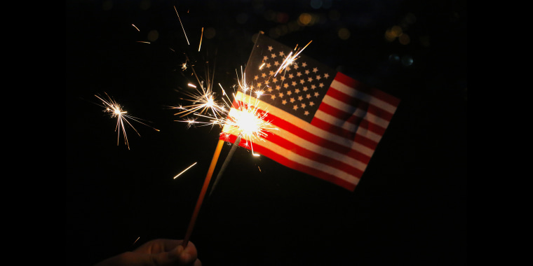 Hand holding a small American flag and lighted sparkler on the Fourth of July