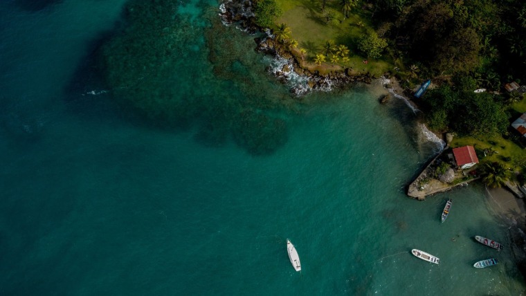 Cinco barcos pequeños navegan sobre un mar azul verdoso cristalino junto a la costa de una playa en Capurganá, parte de la pronvinca colombia del Chocó, el 19 de marzo de 2022
