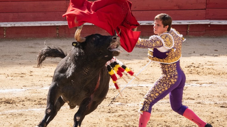 Un torero levanta su capote por sobre un toro que empieza a sangrar durante una corrida de toros