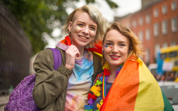 two woman with a rainbow pride flag draped around them