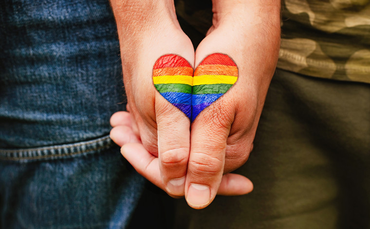 two people holding hands and forming rainbow heart