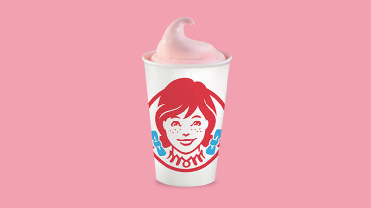A pink frosty in a white cup with the Wendy's logo in front of a pink background.