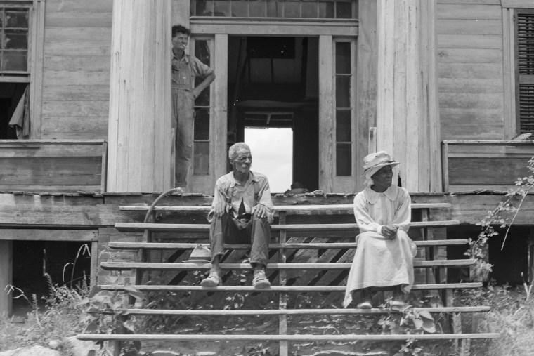 A formerly enslaved man and his wife sit on the steps of a decaying plantation house in Green County, Ga., in 1937.