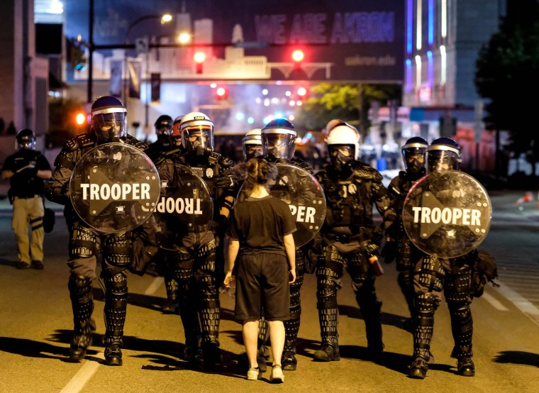 A woman stands in front of troopers in riot gear