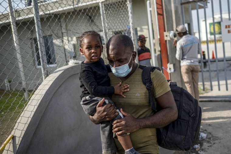 Image: A man deported from the United States carries a baby as they leave the Toussaint Louverture International Airport  on October 28, 2021  in Port-au-Prince, Haiti.