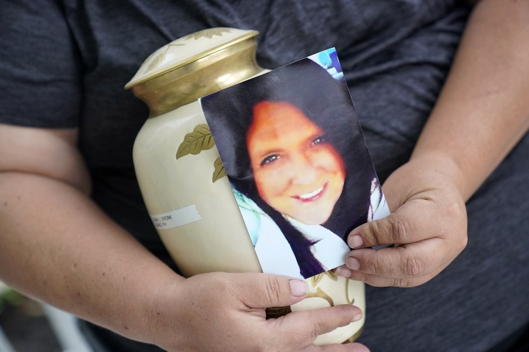 Kelly Titchenell sits on her porch in Mather, Pa., holding a photo of her mother Diania Kronk, and an urn containing her mother's ashes, on July 7, 2022.