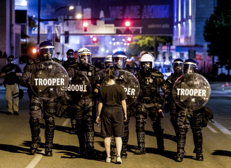 A woman stands in front of soldiers in riot gear as police deploy tear gas and stun grenades to clear the area around Akron City Hall and the Akron Police Station during a protest over the murder of Jayland Walker, in Akron, Ohio on July 3, 2022.