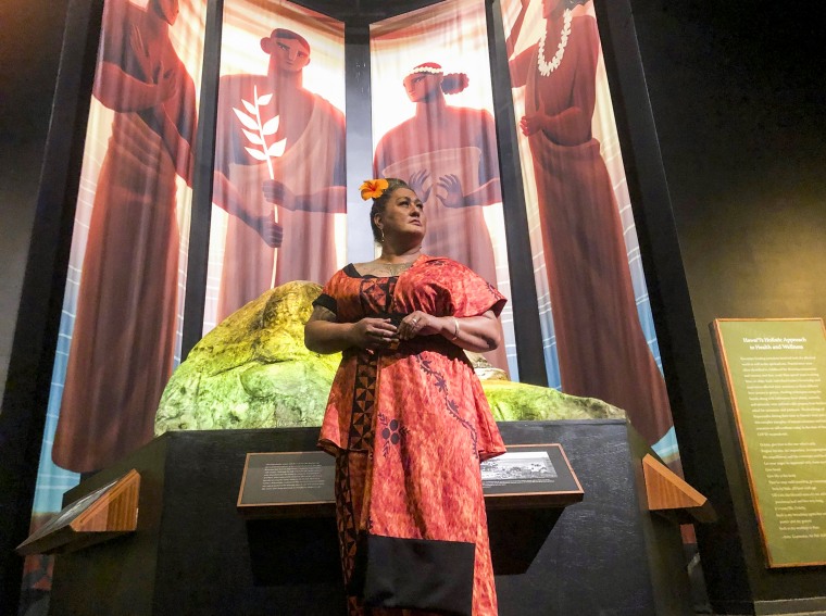 Hinaleimoana Wong-Kalu, one of the curators of the new Kapaemahu exhibit at Bishop Museum, poses for a photo in Honolulu in front of pictures of four healers who visited Hawaii from Tahiti more than 500 years ago, on June 16, 2022.