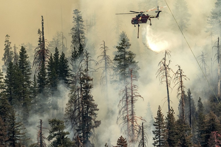 Image: Seen from unincorporated Mariposa County, Calif., a helicopter drops water on the Washburn Fire burning in Yosemite National Park on July 9, 2022.