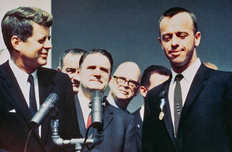 Администраторът на НАСА Джеймс Е. Уеб гледа зад гърба на президента Джон Ф. Кенеди, докато връчва на астронавта Алън П. Шепърд младши наградата на НАСА за изключителни заслуги на Гала в Розовата градина на 8 май 1961 г.