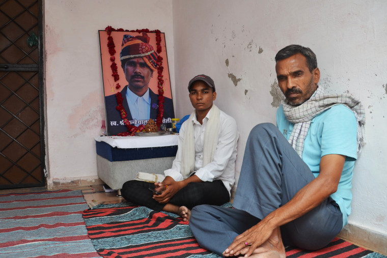Yash Teli, left, next to his slain father’s photo with a relative at his home in Udaipur this month.