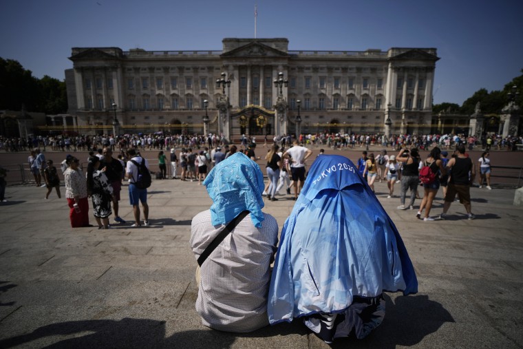 People sit covering their heads from the sun outside Buckingham Palace in London on Monday. 