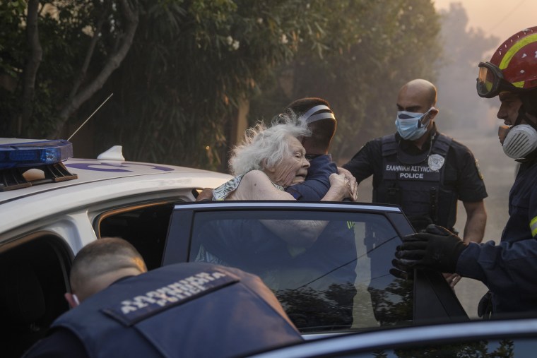 Firefighters and policemen evacuate an elderly woman from her house in Penteli, Greece, on July 19, 2022.