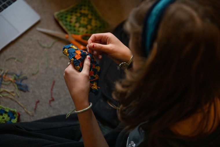 Teenage girl sitting on floor crocheting.