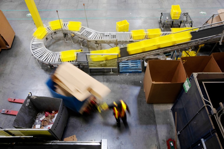 Image: An employee pulls a pallet jack past plastic crates moving along a conveyor at the Amazon.com Inc. fulfillment center in Robbinsville, N.J., on June 7, 2018.