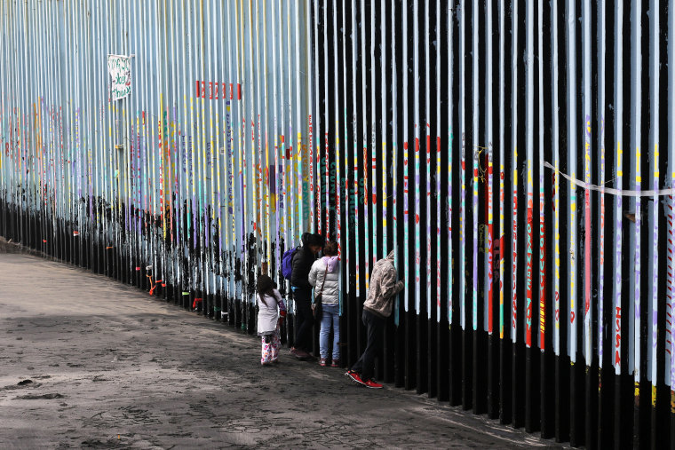 A family of Central American migrants look through the U.S.-Mexico border fence, in Playas de Tijuana, Baja California state, Mexico, on Jan. 16, 2019.