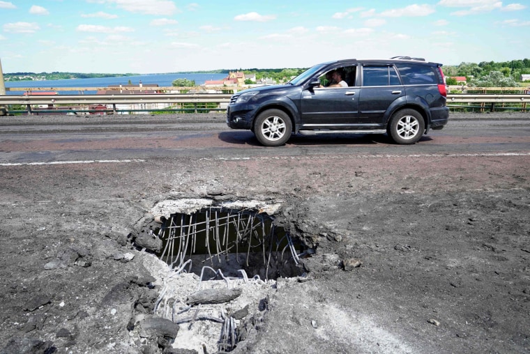 A car drives past a crater caused by a Ukrainian rocket strike on on Kherson's Antonovsky (Antonivskiy) bridge on July 21, 2022.