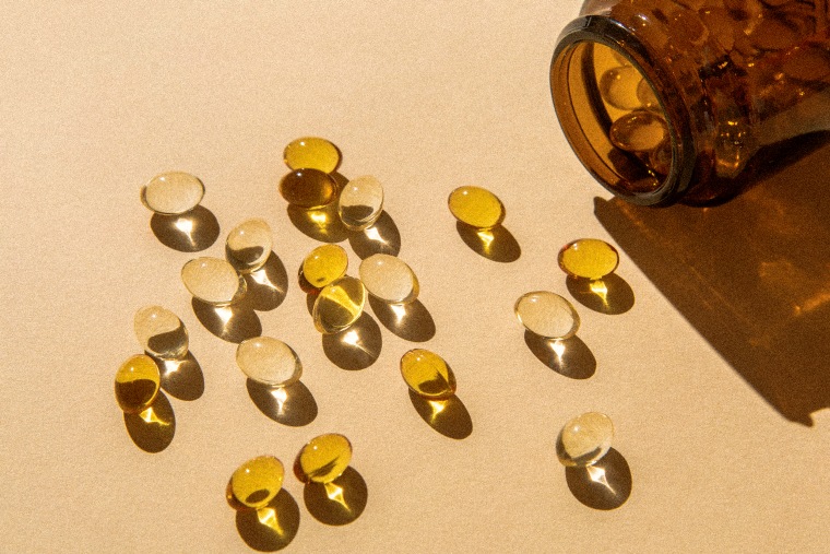 Vitamin D capsules poured out of the bottle on a beige background.