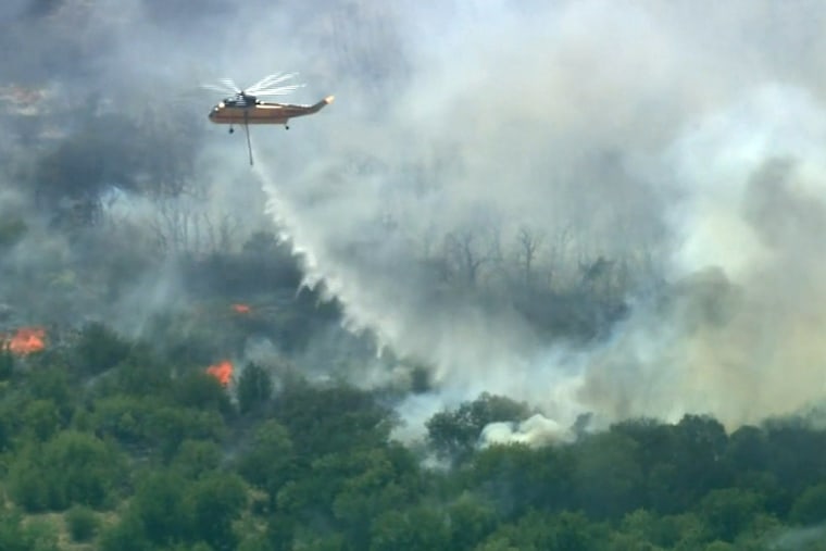 A firefighting helicopter drops water on a fast-moving wildfire that has forced dozens of evacuations in North Texas.