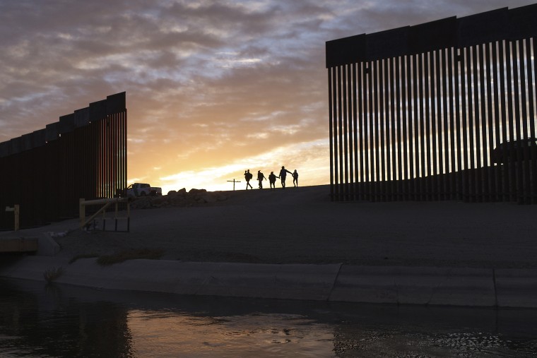 A pair of migrant families from Brazil pass through a gap in the border wall to reach the U.S. in Yuma, Ariz., on June 10, 2021, after having crossed from Mexico to seek asylum.