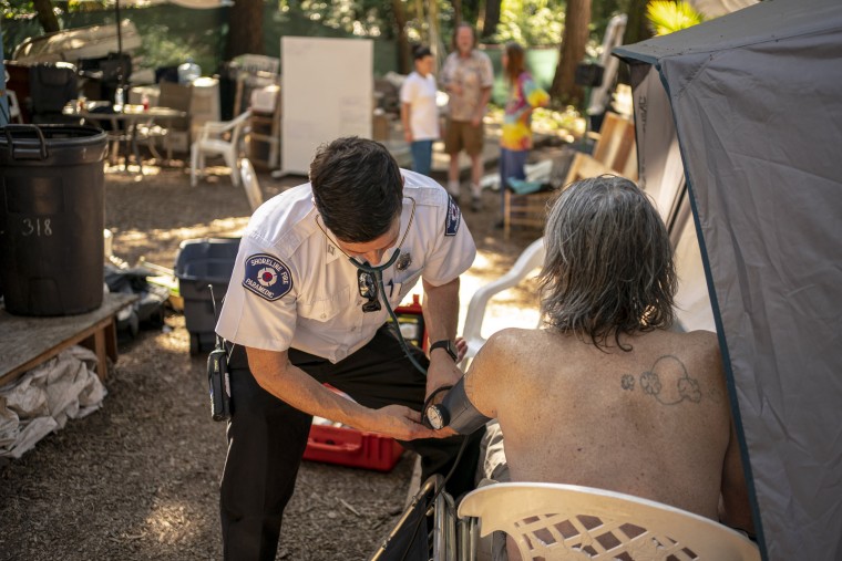 Image: Gabe DeBay, Medical Services Officer with the Shoreline Fire Department, checks the blood pressure of a homeless man at a tent encampment during the hottest part of the day on July 26, 2022 in Shoreline, Wash.