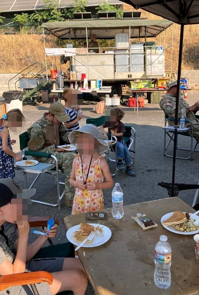 Image: Militia members in military fatigues eat breakfast in the parking lot of H&L Lumber in Mariposa, Calif., on July 24, 2022. Children's faces have been obscured by NBC News.