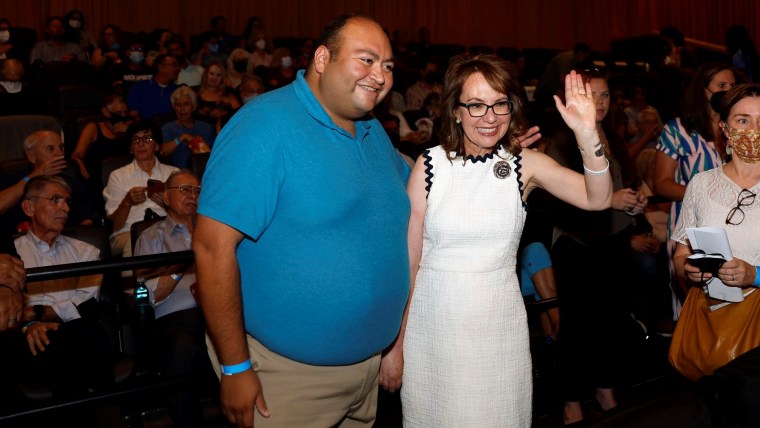 Daniel Hernandez, un hombre de camisa azul y pantalones khakis, posa sonriente junto a Gabrielle Giffords, exlegisladora por Arizona que tiene un vestido blanco y anteojos