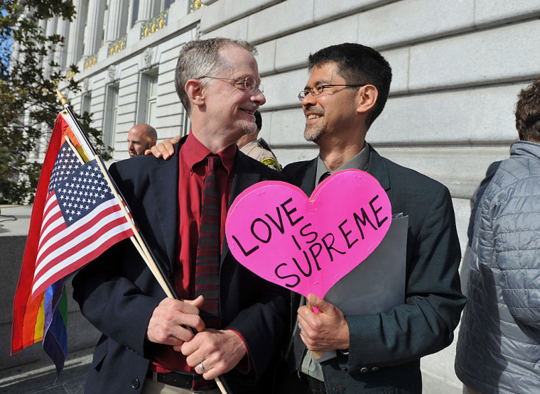 John Lewis, a la izquierda, y su marido Stuart Gaffney, demandantes en el caso de la Ley de Defensa del Matrimonio (DOMA) de 2008, sostienen banderas y un cartel en el que se lee 'Love is Supreme' tras la sentencia del la Corte Suprema de Estados Unidos sobre el matrimonio entre personas del mismo sexo, el viernes 26 de junio de 2015.