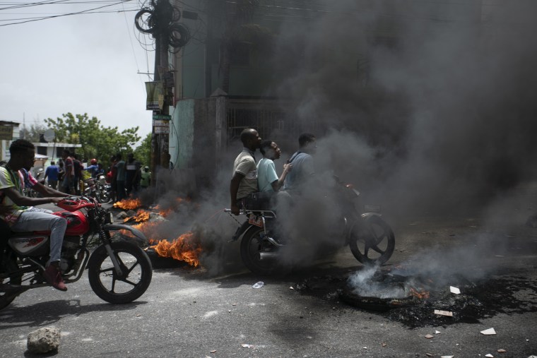 Un mototaxista transporta pasajeros a través de una barricada para protestar por el aumento del precio de la gasolina en Puerto Príncipe, Haití, el 13 de julio de 2022.