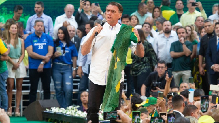 Jair Bolsonaro sostiene una bandera de Brasil y un micrófono durante un evento de campaña