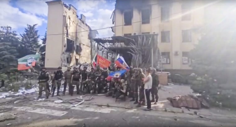 Tropas rusas entre las que hay soldados de un regimiento checheno ondean banderas rusas y chechenas mientras posan para una foto ante un edificio destruido en Lysychansk, Ucrania, el sábado 2 de julio de 2022.
