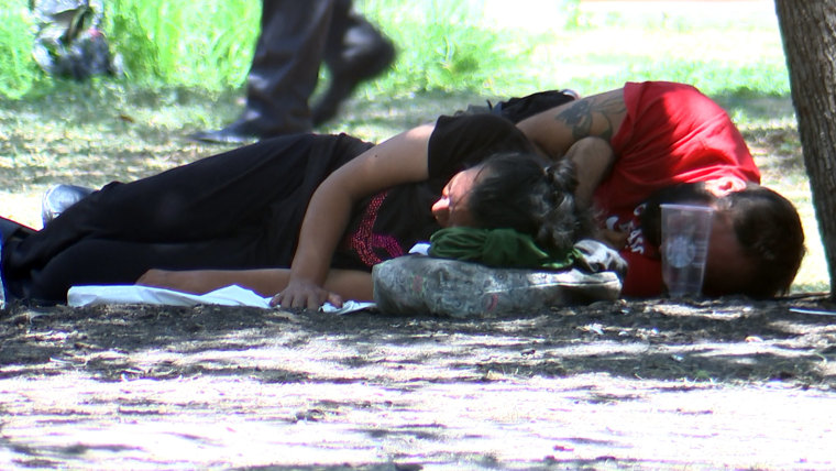 Unos migrantes descansan un mediodía de julio, a más de 100 grados Fahrenheit, en un parque en San Antonio, Texas.