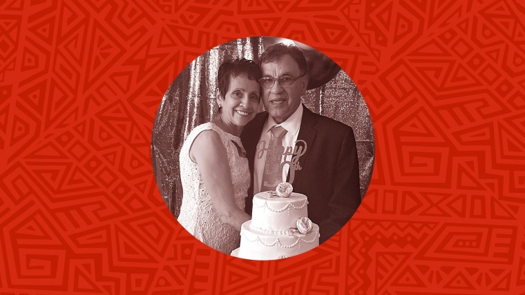 Una pareja de mujer con vestido blanco y hombre con traje posa detrás de un pastel que dice "Feliz 50 aniversario"