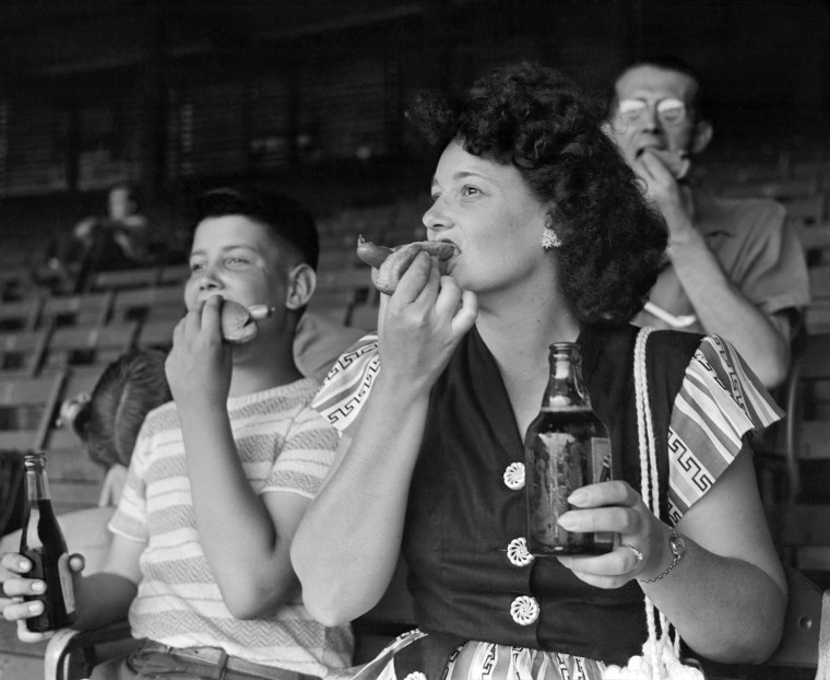 A vintage photo of baseball fans enjoying hot dogs at a game.