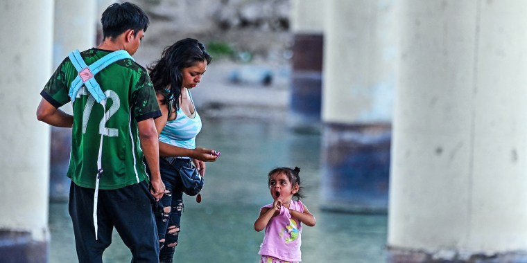 A child looks at a woman and man as they are apprehended near the border with Mexico by US Border Patrol and National Guard troops in Eagle Pass, Texas, on June 30, 2022.