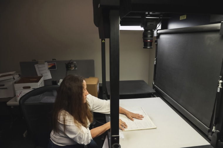 A tracing center worker takes photographs of old gun records that cannot be scanned.