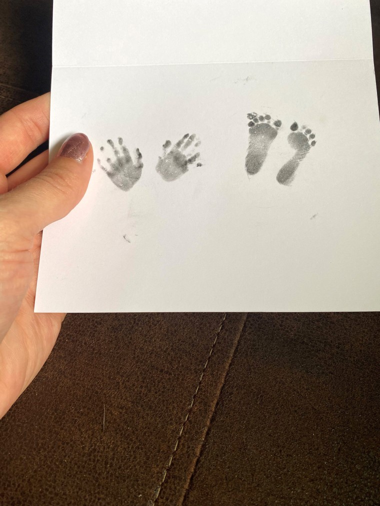 Melissa Janssen holds a paper card with her child's hand and foot prints.