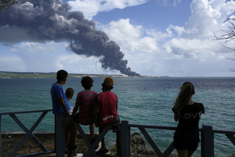 Människor tittar på en enorm uppstigande rökplym orsakad av en brand vid Matanzas Supertanker Base, i Matazanas, Kuba, lördagen den 6 augusti 2022.