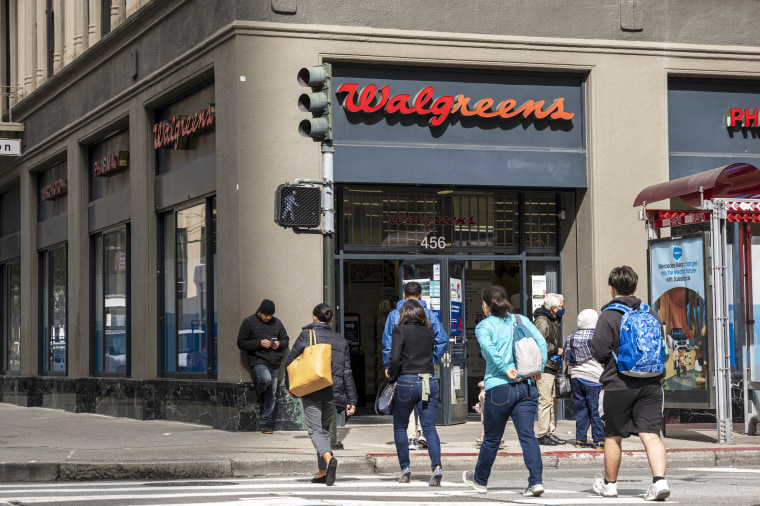 People walk in front of a Walgreens store