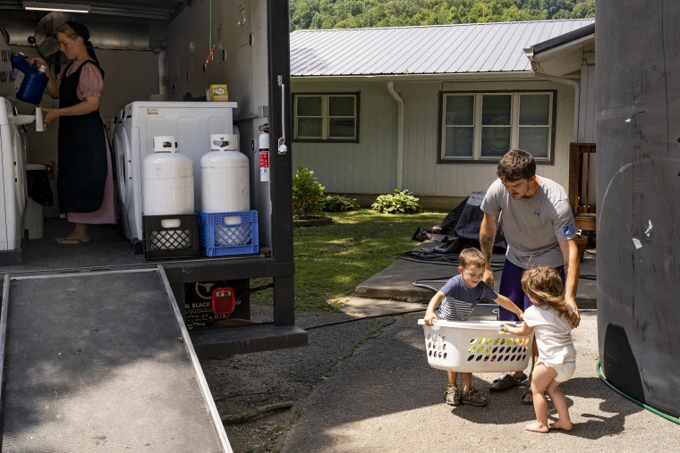 Image: Dillion Hall, right, and his two children, carry a basket of clothes to a laundry truck in downtown Buckhorn, Ky. on Aug. 19, 2022.