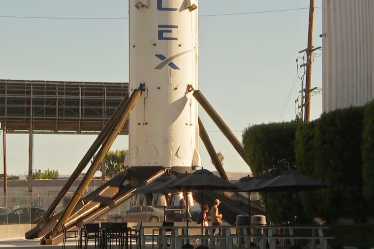 People walk past a SpaceX rocket on display outside SpaceX headquarters in Hawthorne, Calif.