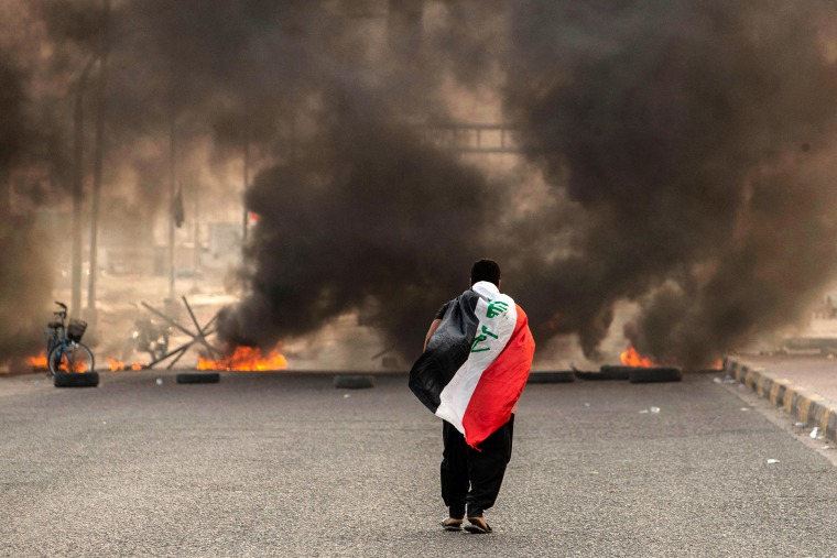 Image: A supporter of Iraqi Shiite cleric Moqtada Sadr carries the Iraqi flag as he walks down a road blocked by burning tires during a demonstration in Iraq's southern city of Basra on Aug. 29, 2022.
